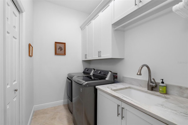 clothes washing area with light tile patterned floors, baseboards, cabinet space, a sink, and washer and clothes dryer