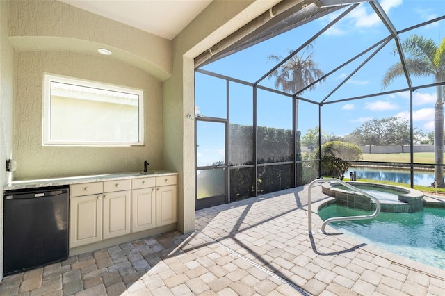 interior space with an outdoor kitchen, a pool with connected hot tub, a sink, a water view, and a lanai