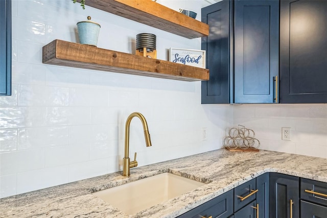 kitchen featuring blue cabinets, tasteful backsplash, open shelves, and a sink