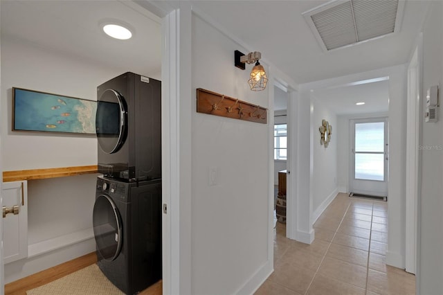 clothes washing area featuring stacked washer and dryer, laundry area, light tile patterned floors, baseboards, and visible vents