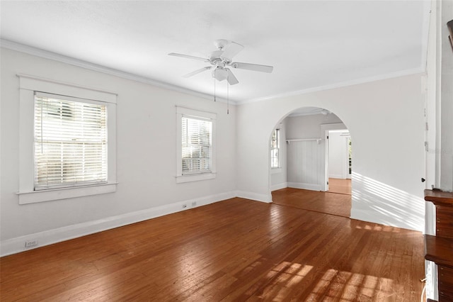 empty room featuring baseboards, arched walkways, hardwood / wood-style flooring, ceiling fan, and crown molding