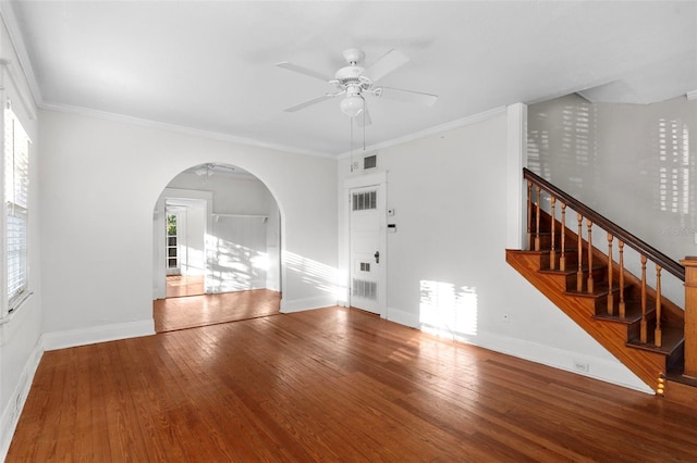 unfurnished room with baseboards, arched walkways, hardwood / wood-style floors, stairs, and crown molding