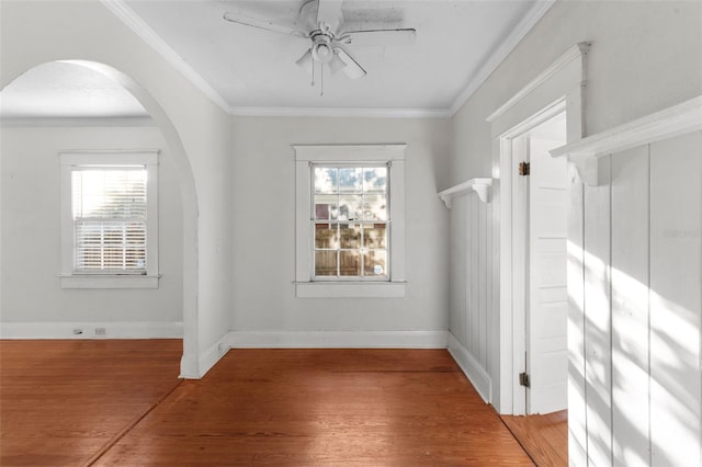 unfurnished room with arched walkways, baseboards, crown molding, and light wood finished floors