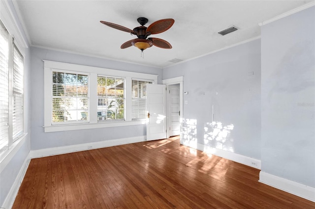 empty room with baseboards, wood finished floors, visible vents, and crown molding