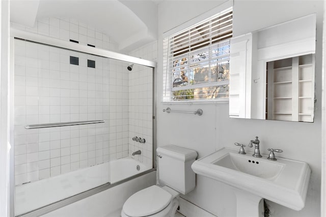 full bathroom featuring toilet, bath / shower combo with glass door, and a sink