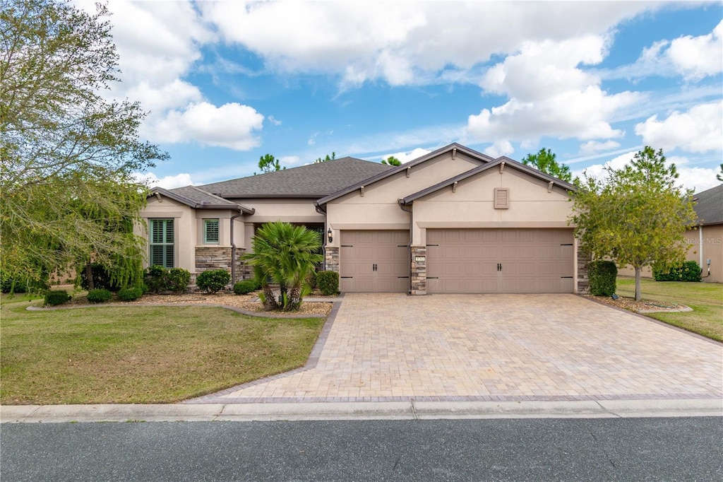 ranch-style house featuring decorative driveway, stucco siding, a front yard, a garage, and stone siding