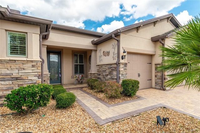 entrance to property featuring a garage, stone siding, and stucco siding