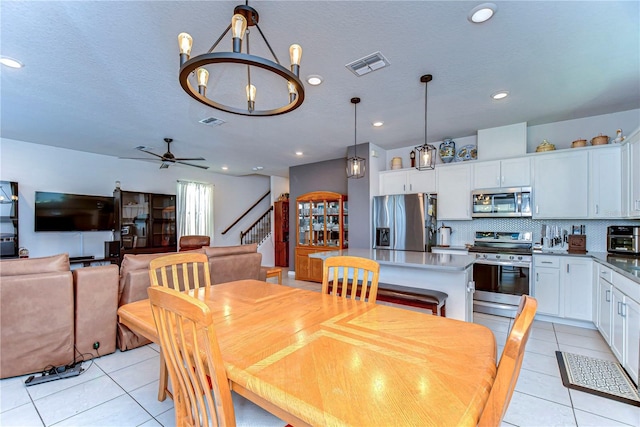 dining room with light tile patterned flooring, visible vents, ceiling fan with notable chandelier, and stairs