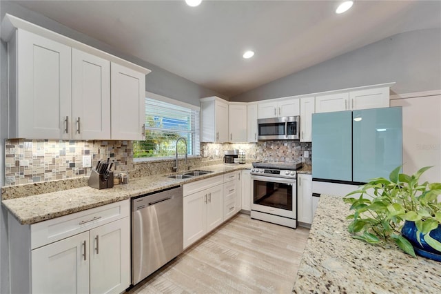 kitchen with light wood-style flooring, a sink, appliances with stainless steel finishes, white cabinets, and vaulted ceiling