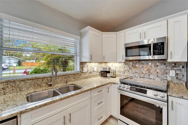 kitchen with a sink, tasteful backsplash, appliances with stainless steel finishes, white cabinets, and vaulted ceiling