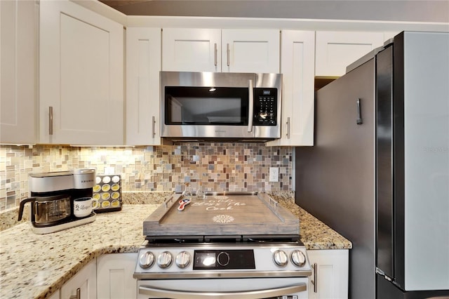 kitchen featuring decorative backsplash, white cabinets, light stone counters, and appliances with stainless steel finishes