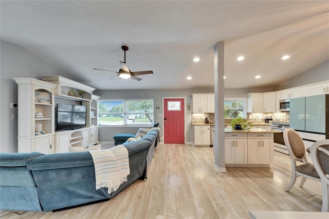 living room featuring a healthy amount of sunlight, lofted ceiling, light wood-style floors, and ceiling fan