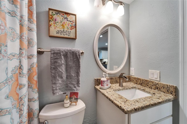 bathroom with curtained shower, toilet, vanity, and a textured wall