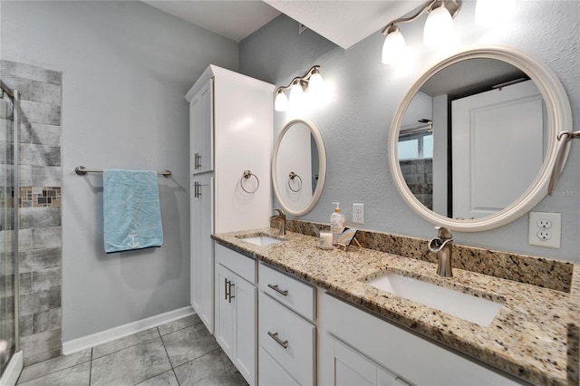 bathroom with a tile shower, double vanity, baseboards, and a sink