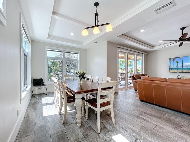 dining space featuring baseboards, a tray ceiling, visible vents, and light wood-style floors