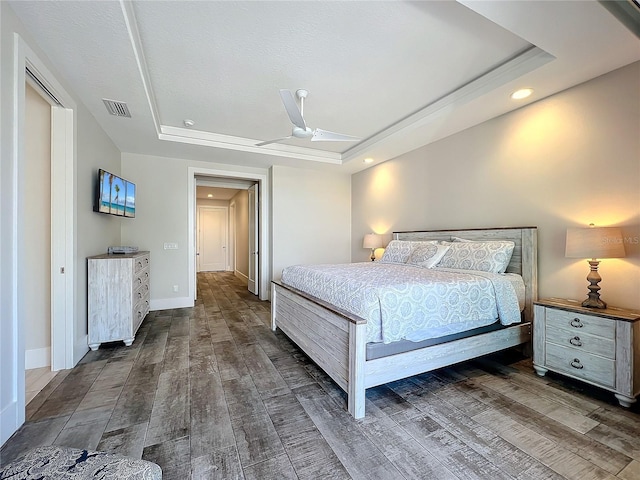 bedroom with a tray ceiling, wood finished floors, visible vents, and baseboards