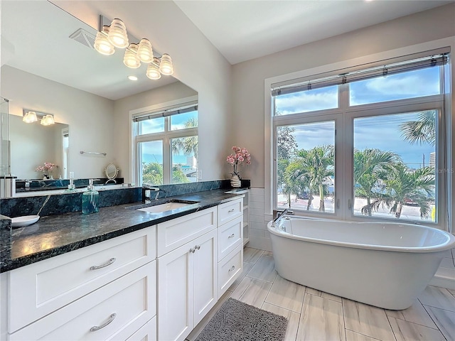 full bath featuring tile walls, a soaking tub, plenty of natural light, and vanity