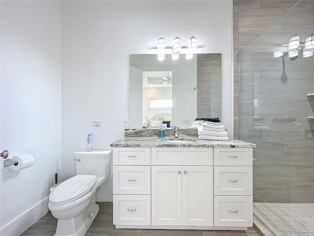 bathroom with baseboards, a tile shower, vanity, and toilet