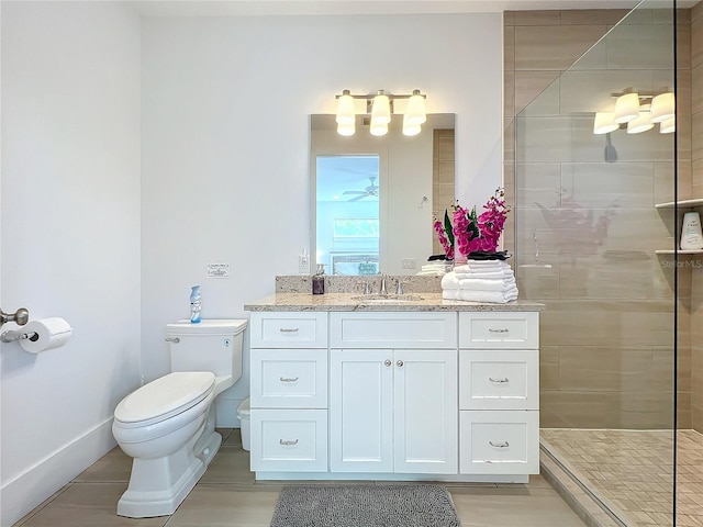 full bathroom with toilet, a ceiling fan, a tile shower, vanity, and baseboards