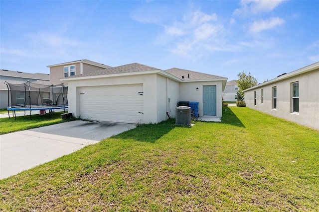 exterior space with a trampoline, concrete driveway, a lawn, central AC, and a garage