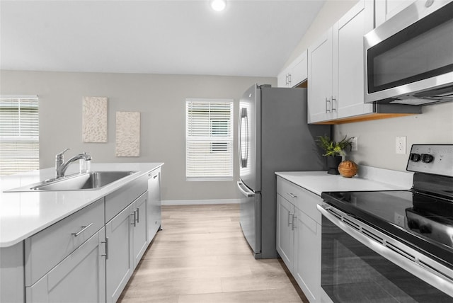 kitchen featuring light wood-style flooring, a sink, baseboards, light countertops, and appliances with stainless steel finishes