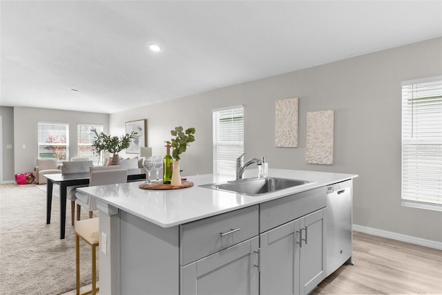 kitchen with dishwasher, open floor plan, a kitchen island with sink, light countertops, and a sink