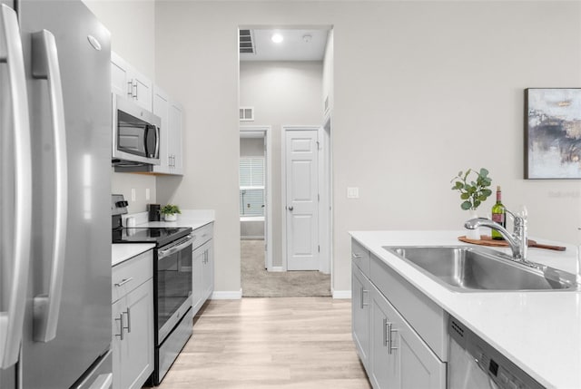 kitchen featuring baseboards, light wood-style flooring, stainless steel appliances, light countertops, and a sink