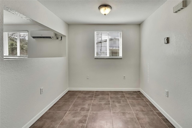 tiled empty room featuring a wall unit AC, baseboards, and a textured wall