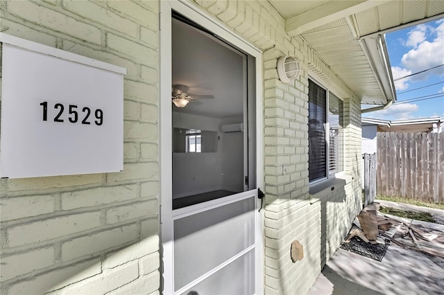 doorway to property featuring fence, an AC wall unit, and brick siding