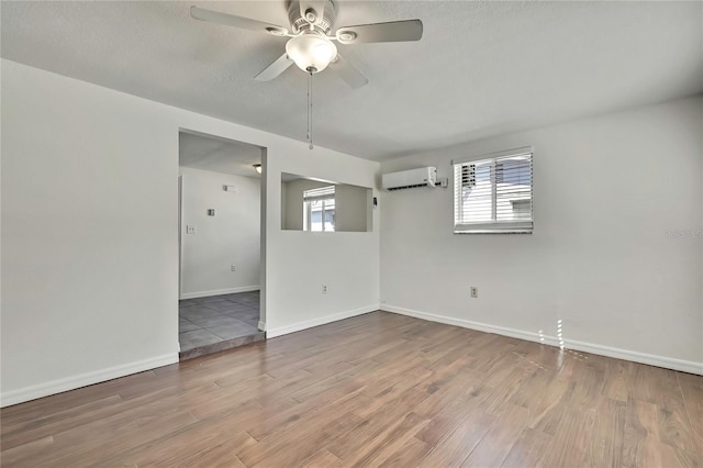 spare room featuring baseboards, a wall unit AC, ceiling fan, wood finished floors, and a textured ceiling