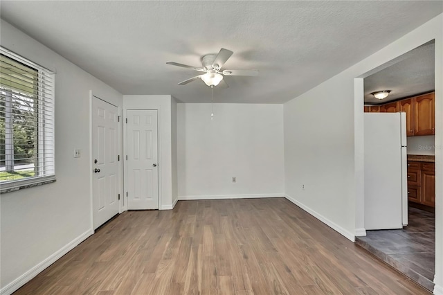 interior space featuring a ceiling fan, a textured ceiling, baseboards, and wood finished floors