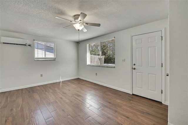 empty room featuring baseboards, a ceiling fan, a wall unit AC, wood finished floors, and a textured ceiling