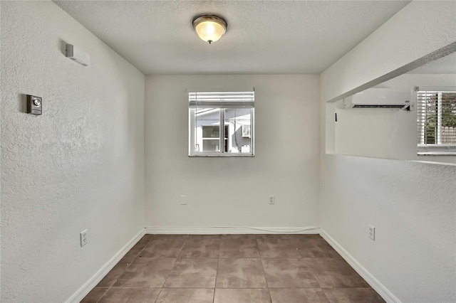 spare room featuring a textured ceiling, a textured wall, tile patterned flooring, baseboards, and an AC wall unit