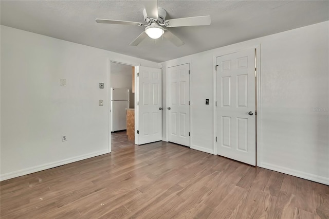 unfurnished bedroom featuring baseboards, a ceiling fan, freestanding refrigerator, and light wood-style floors