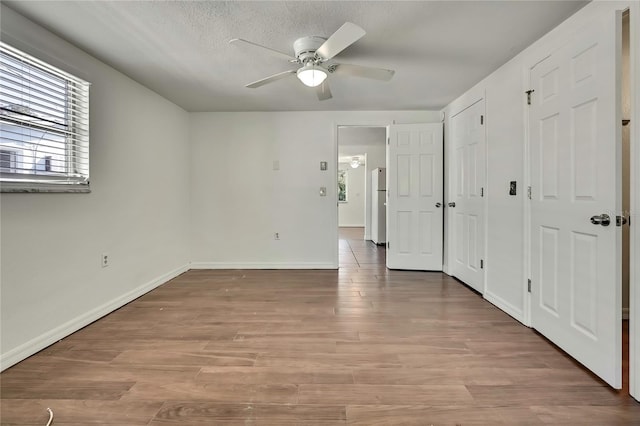 unfurnished bedroom featuring ceiling fan, a textured ceiling, wood finished floors, baseboards, and freestanding refrigerator