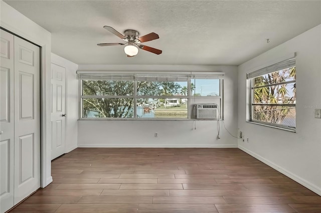 unfurnished bedroom featuring a textured ceiling, cooling unit, wood finished floors, and baseboards