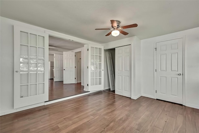 unfurnished bedroom featuring a closet, freestanding refrigerator, ceiling fan, wood finished floors, and baseboards