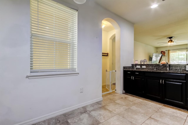 kitchen with dark cabinets, arched walkways, baseboards, and dark stone countertops