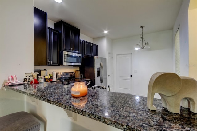 kitchen with stainless steel appliances, a breakfast bar, hanging light fixtures, dark cabinetry, and dark stone countertops