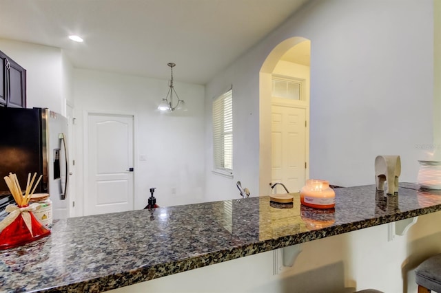 kitchen with arched walkways, a breakfast bar area, a peninsula, stainless steel refrigerator with ice dispenser, and pendant lighting