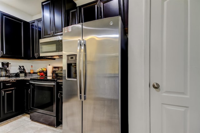 kitchen with appliances with stainless steel finishes, dark stone counters, dark cabinetry, and light tile patterned flooring