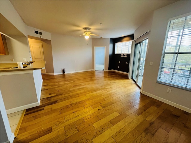 unfurnished living room featuring a wealth of natural light, wood-type flooring, visible vents, and ceiling fan