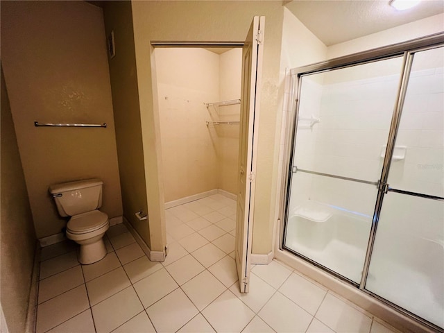 bathroom with toilet, a stall shower, a walk in closet, and tile patterned floors