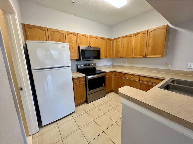 kitchen with light tile patterned floors, light countertops, appliances with stainless steel finishes, brown cabinetry, and a sink