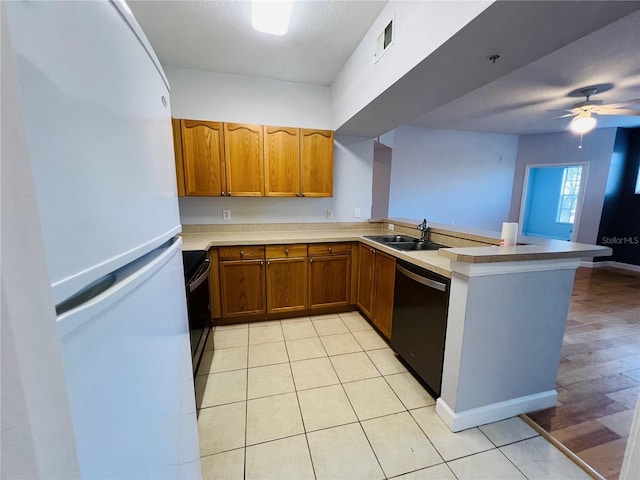 kitchen featuring freestanding refrigerator, dishwashing machine, a sink, a peninsula, and brown cabinetry