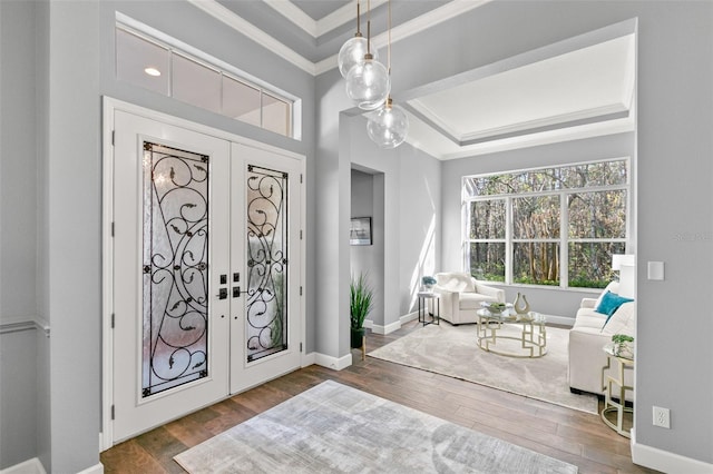 entrance foyer with a raised ceiling, crown molding, wood-type flooring, and french doors