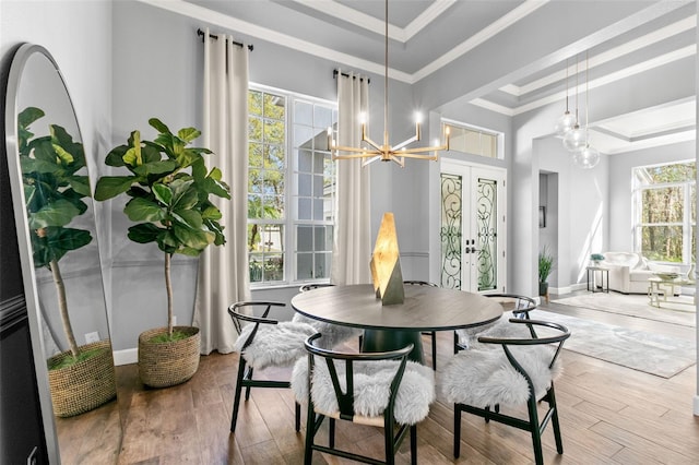 dining space featuring wood finished floors, french doors, an inviting chandelier, a raised ceiling, and crown molding