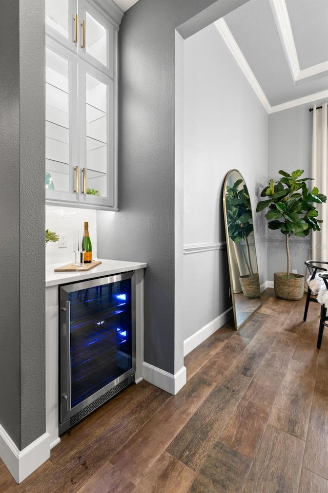 bar featuring a bar, wine cooler, ornamental molding, and dark wood-type flooring