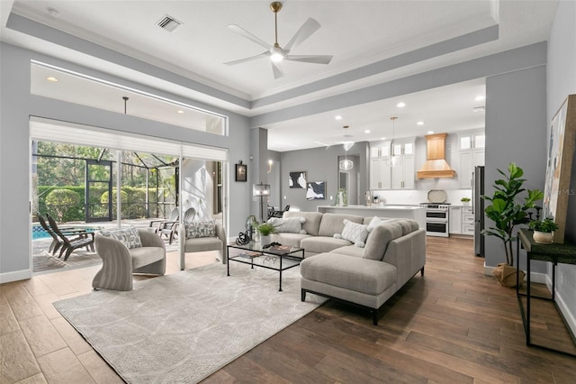 living area with dark wood-style floors, a tray ceiling, visible vents, ornamental molding, and baseboards