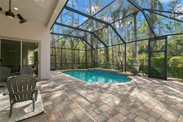 pool with a patio, glass enclosure, and a ceiling fan